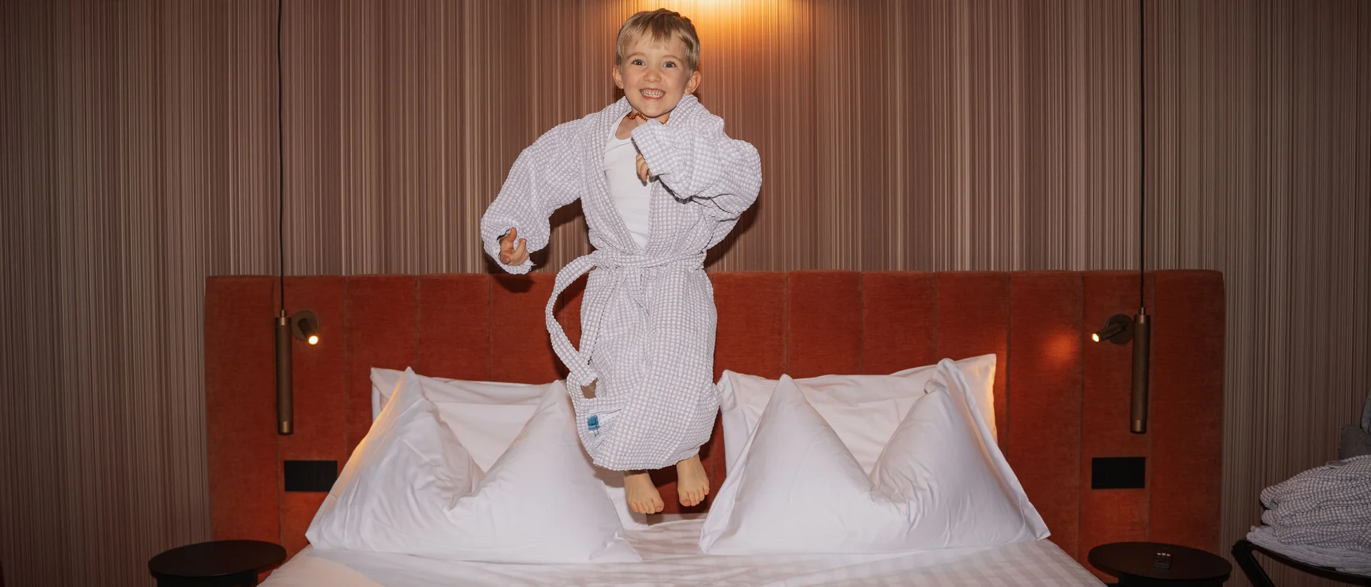 Elgus: hotel a San Giacomo, a Brentonico Bambino che salta su un letto in una stanza d'albergo moderna
